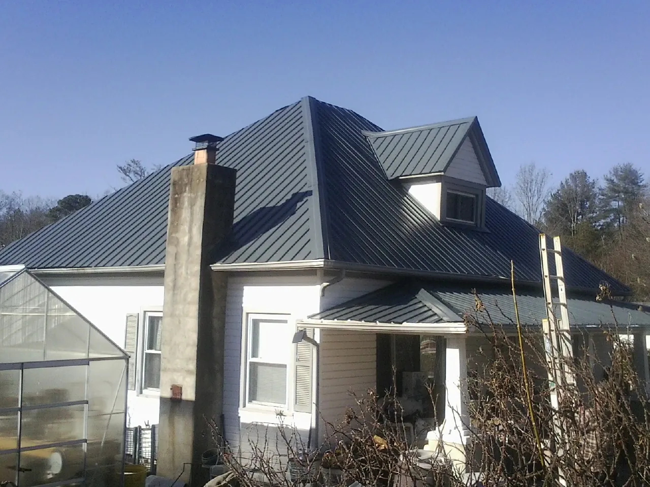 Dark blue standing seam metal roof on a white farmhouse with dormer — Slate & Tile Roof Repair by Roofing Brothers in Jamestown